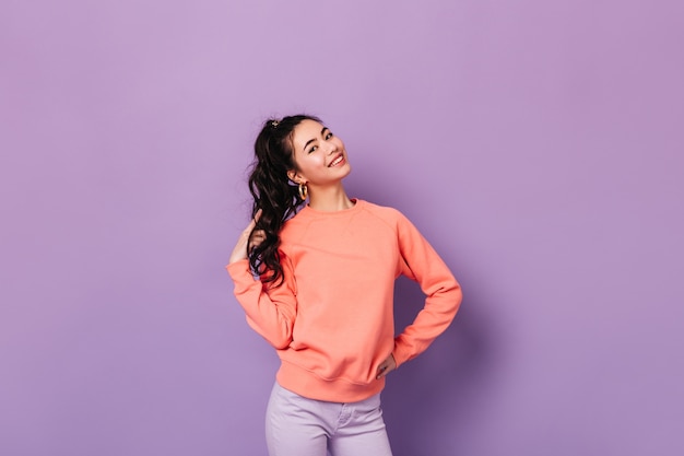 Joyful korean woman posing with hand on hip. studio shot of stunning asian young lady playing with curly hair. Free Photo