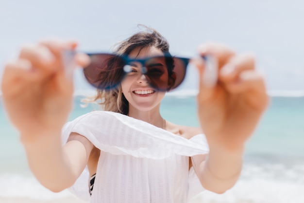 海でサングラスをかけてふざけてポーズをとるうれしそうな日焼けした女性 ビーチで浮気しているかなり若い女性の屋外写真 無料の写真