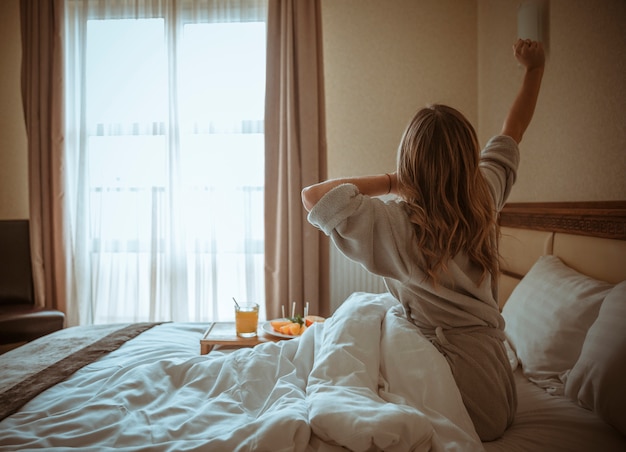 Junge Frau sitzt woman auf dem Bett und streckt ihre Hand beim Frühstück auf dem Tisch Kostenlose Fotos