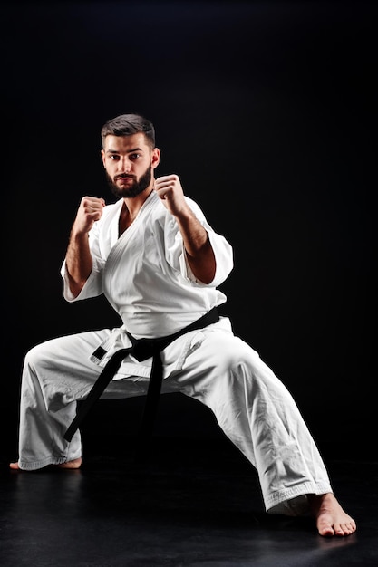 Premium Photo | Karate man in a kimono in fighting stance on a black ...