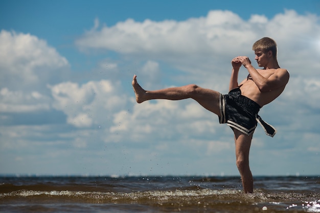 Kickboxer kicks in the open air in summer against the sea. Premium Photo