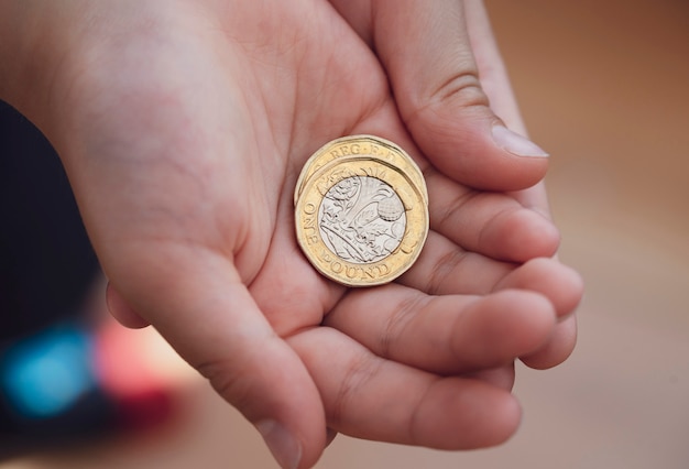 子供の手に彼の手に2ポンド硬貨 両手に新しいイギリスの1ポンドを保持している子供 ニューポンド硬貨 17年デザイン プレミアム写真