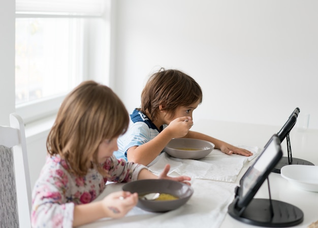 Premium Photo | Kids in dining room eating and watching tablet