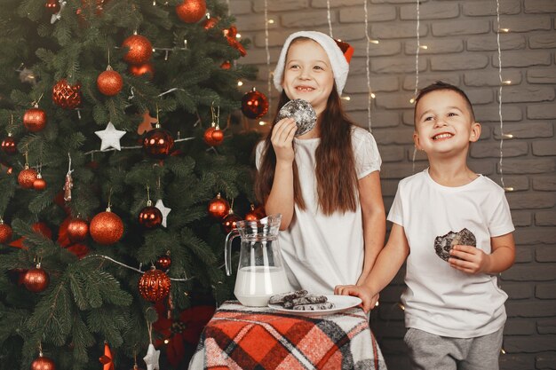 クリスマスツリーの近くに立っている子供たち 牛乳と一緒にクッキーを食べる子供たち 無料の写真