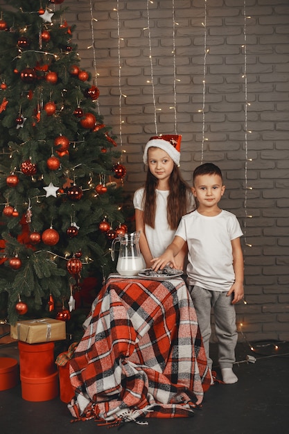 クリスマスツリーの近くに立っている子供たち 牛乳と一緒にクッキーを食べる子供たち 無料の写真