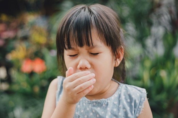 Kids using hand covering her mouth while cough which is incorrect sneezing. Premium Photo