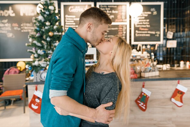 カフェでクリスマスツリーの近くの若いカップルのキス プレミアム写真