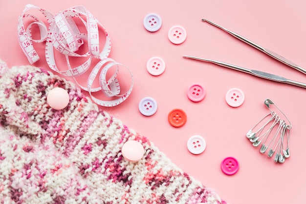Knitting crochet; measuring tape; buttons; safety pins and needles on pink backdrop Free Photo