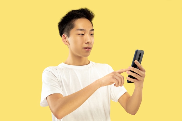 Free Photo Korean Young Man S Half Length Portrait On Yellow Studio Background Male Model In White Shirt Using Smartphone Concept Of Human Emotions Facial Expression Front View Trendy Colors