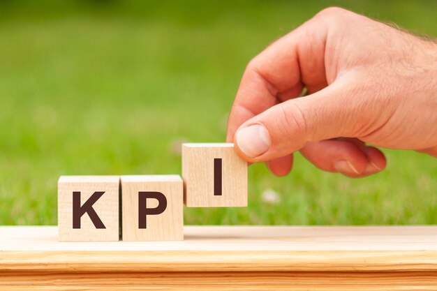  Kpi is a word written on wooden blocks. a man's hand holds a wooden cube with the letter i from the