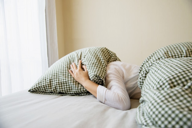 Lady cover her head by pillow on a bed Free Photo