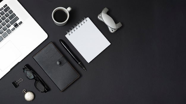 オフィス文具と黒の背景上の紅茶のカップとパーソナルアクセサリーのラップトップ 無料の写真