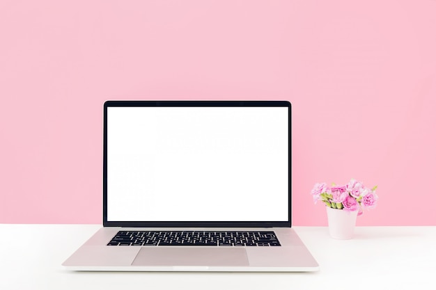 白い空白の画面とピンクの背景のテーブルの上に花瓶に花とノートパソコン プレミアム写真