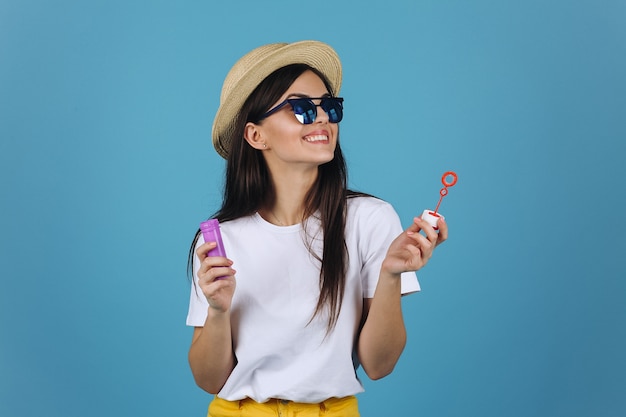 Laughing brunette girl in summer hat and sunglasses has fun with soap balloons Free Photo