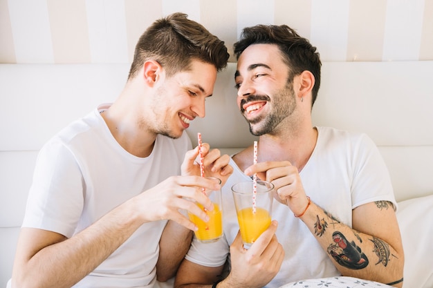 ベッドでジュースを楽しんで笑っているゲイカップル 無料の写真