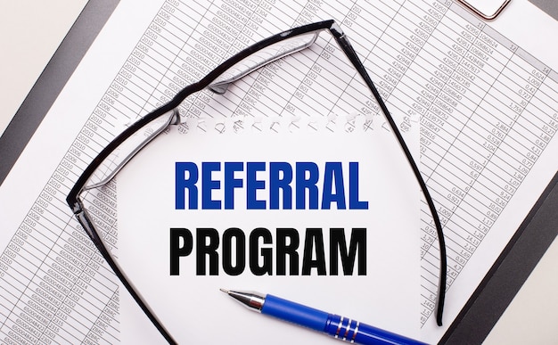 Premium Photo On A Light Background A Report Black Framed Glasses A Pen And A Sheet Of Paper With The Text Referral Program Business Concept