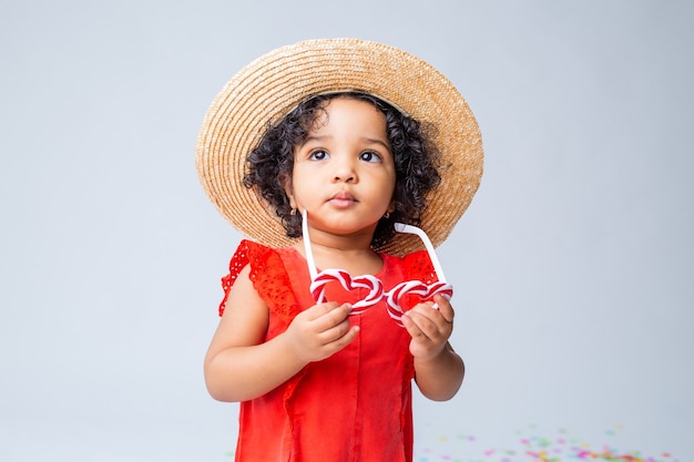 Little african american girl in red summer clothes and a straw hat on a white background in the studio Premium Photo