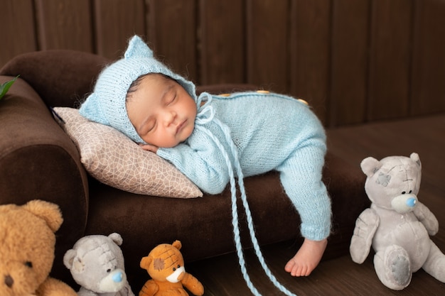 小さな赤ちゃん男の子かわいい新生児幼児のおもちゃに囲まれた青いかぎ針編みのピジャマの茶色のソファの上に敷設 無料の写真