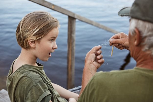 小さな男の子が父親と一緒に釣りをしていて 釣り竿のもつれたラインに驚いて 水に通じる木製の階段でポーズをとっている家族は 男性の子供を驚かせました 無料の写真