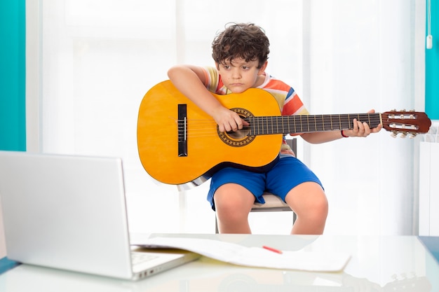 Premium Photo Little Boy At Home Playing The Spanish Guitar In Front Of His Laptop