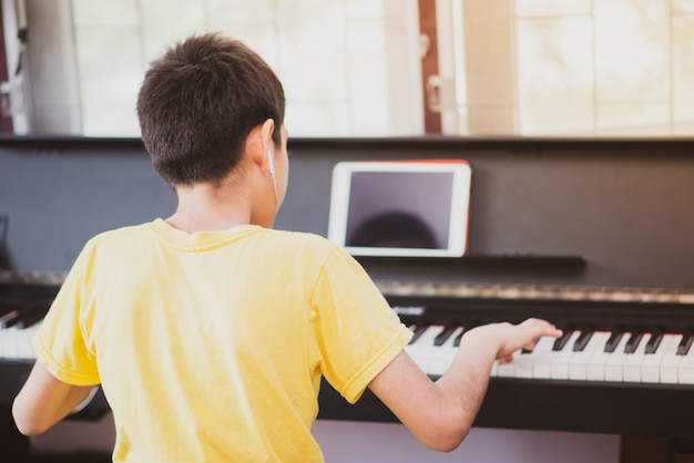 自宅でピアノオンラインデジタルタブレットを練習する小さな男の子 プレミアム写真