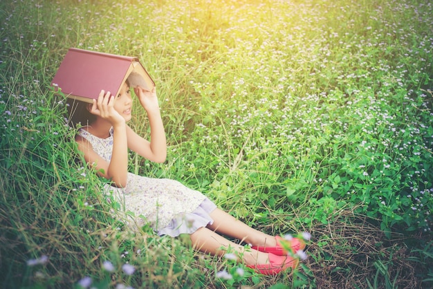 Little Cute Asian Girl Cover Book On Her Head At Nature Free Photo