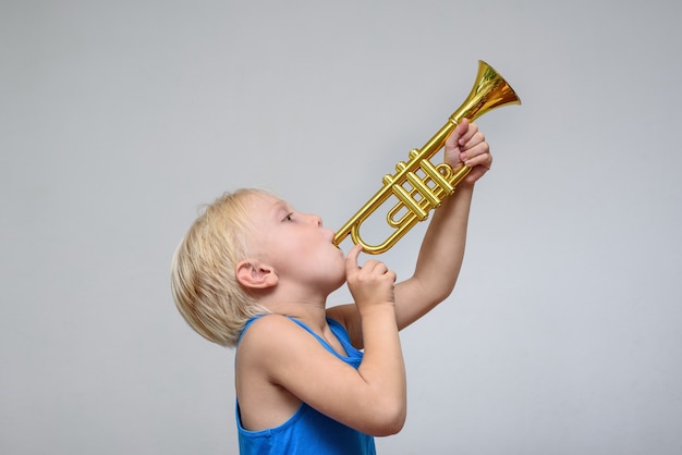 光の壁でおもちゃのトランペットを演奏する小さなかわいい金髪の少年 プレミアム写真