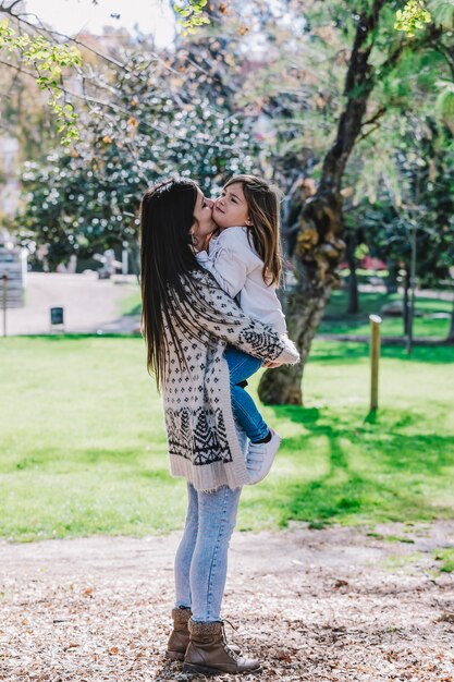 小さなかわいい子女の赤ちゃんが頬にキスし 緑豊かな公園で幸せなきれいな女性と抱擁を抱きしめます プレミアム写真