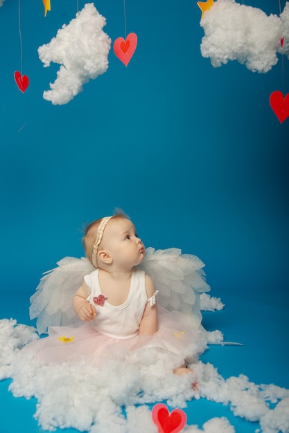バレンタインデーの青い背景の上の小さなかわいい女の子の天使 プレミアム写真