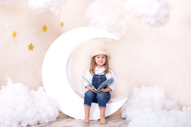 雲と星と月に座っているかわいい女の子 子供は読むことを学びます 少女は本を手に読んでいます 子供は夢を見ています 子供は子供部屋で学び 遊ぶ 学校 プレミアム写真
