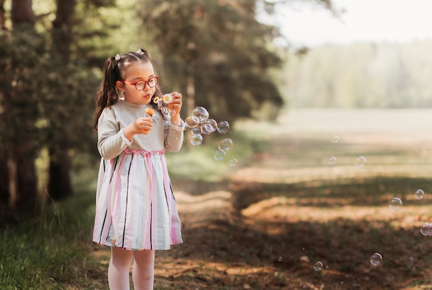 小さな面白い女の子は夏に自然の中でシャボン玉で遊ぶ プレミアム写真