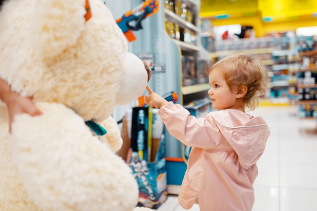 Premium Photo | Little girl choosing big teddy bear in kids store, side ...