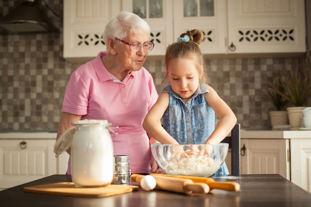 Premium Photo | Little girl and her grandmother cooking in the kitchen