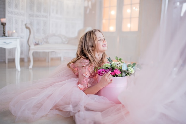 ピンクのドレスの少女は 豪華な部屋の床に座っているバラの箱を保持 無料の写真