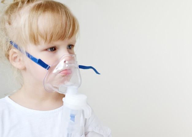 Little girl in a mask for inhalations, making inhalation with nebulizer at home inhaler on the table, indoor, sick child Premium Photo