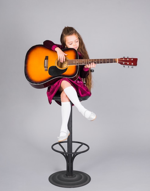 小さな女の子がバーの椅子にアコースティックギターを弾く プレミアム写真