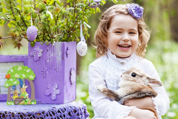 Little girl  playing with real rabbit in the garden. laughing child at easter egg hunt with  pet bunny. spring outdoor fun for kids with pets Premium Photo