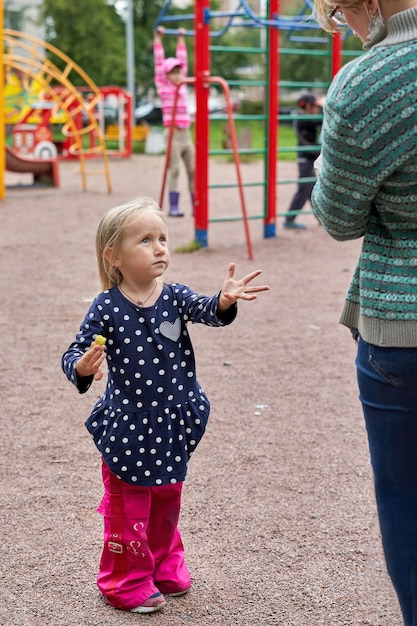 小さな女の子は子供の遊び場の背景に食べ物を求めて母親に手を引っ張る プレミアム写真