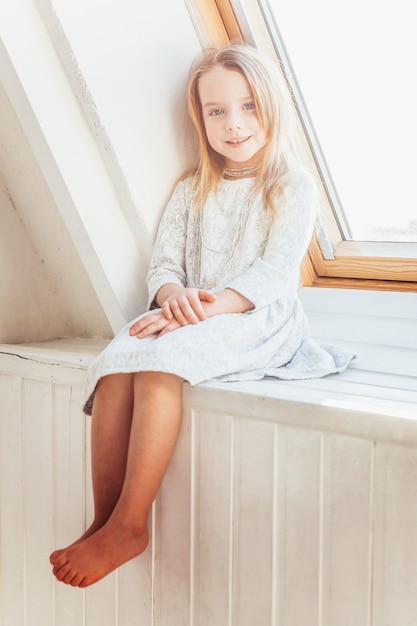 Premium Photo | Little girl sitting on window sill in bright light ...