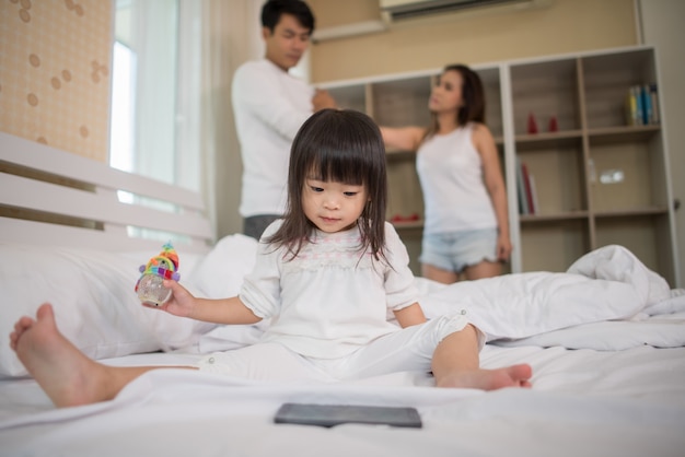 Little girl sitting with her parents on the bed looking serious Free Photo