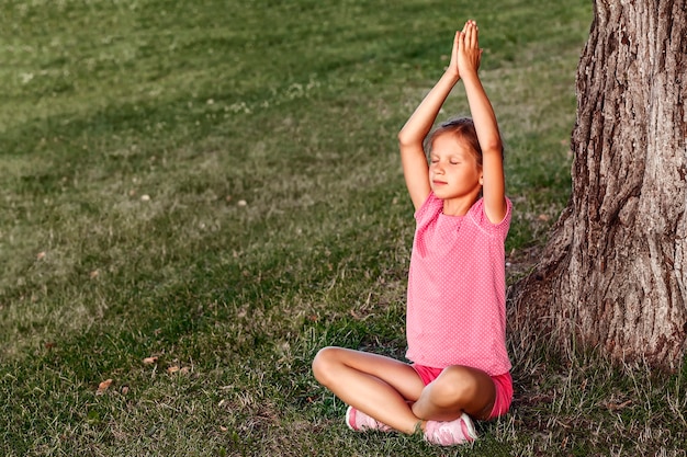 Premium Photo | Little girl sitting in a yoga pose on the grass