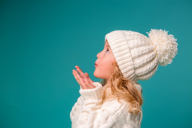 Little girl in white winter knitted hat and sweater on blue Premium Photo