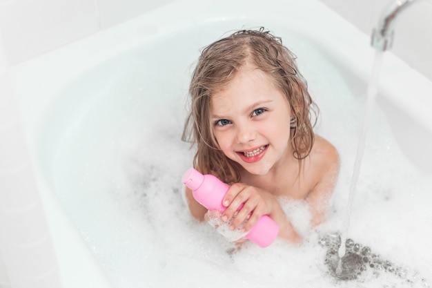 Little Happy Girl In The Bathroom With Foam And With Shampoo Bottles  Premium Photo