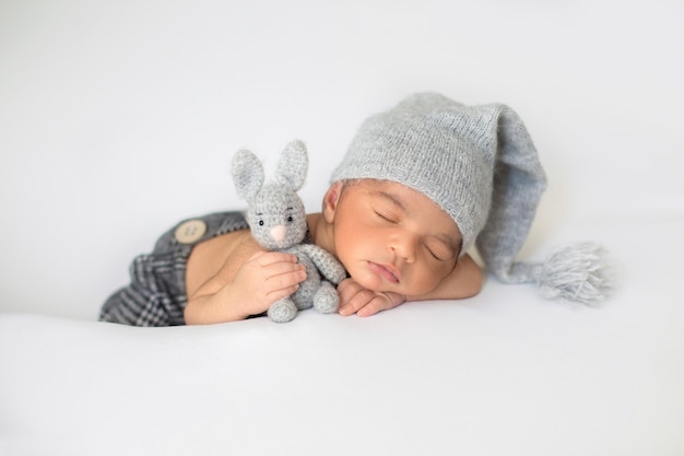 Little infant sleeping with cute grey hat and with toy rabbit in his hands Free Photo