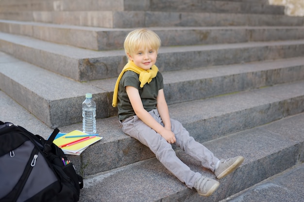 Little student sitting on staircase near the school building. Premium Photo