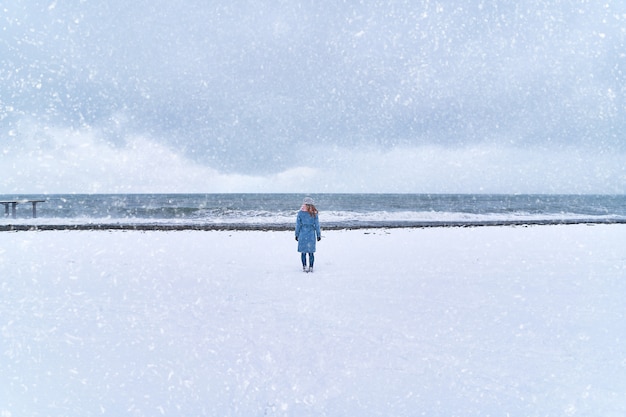 孤独な女性が雪の海岸の吹雪に立っています プレミアム写真