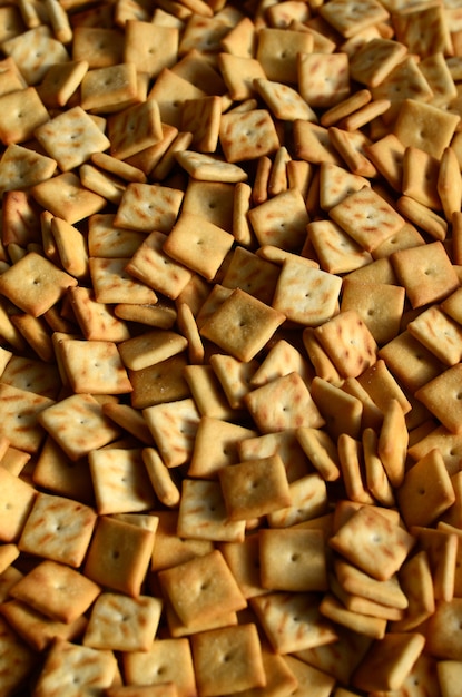 A lot of small cookies are square shaped. a pattern of a yellow salt cracker. background image with salted pastry Premium Photo