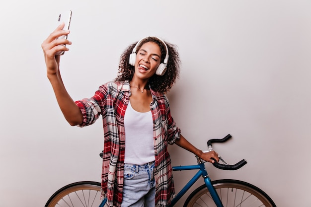 青い自転車の横で自分撮りをしている素敵な女の子 自分の写真を撮りながら浮気しているかなりアフリカの女性のスタジオショット 無料の写真