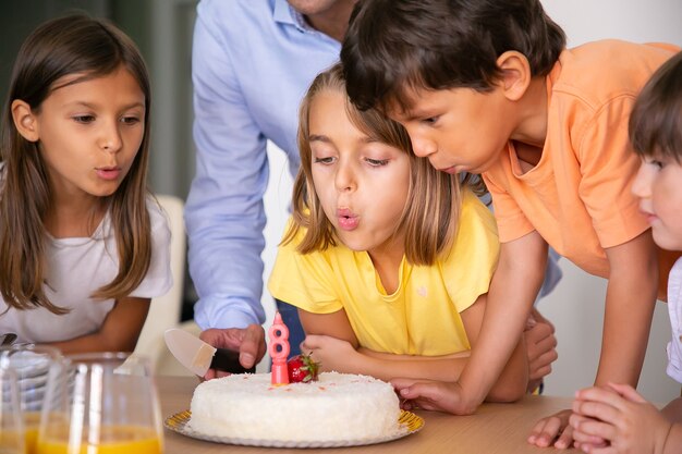 ろうそくを吹き消して願い事をする素敵な子供たち 友人やケーキと彼女の誕生日を祝う金髪の白人の女の子 一緒に楽しんで幸せな子供たち 子供の頃 お祝い 休日の概念 無料の写真