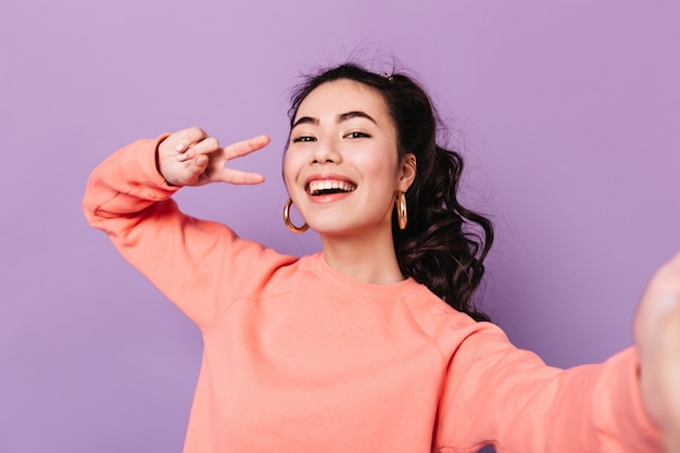 ピースサインでポーズをとる素敵な韓国人女性 紫の背景でselfieを撮って笑うアジアの若い女性 無料の写真